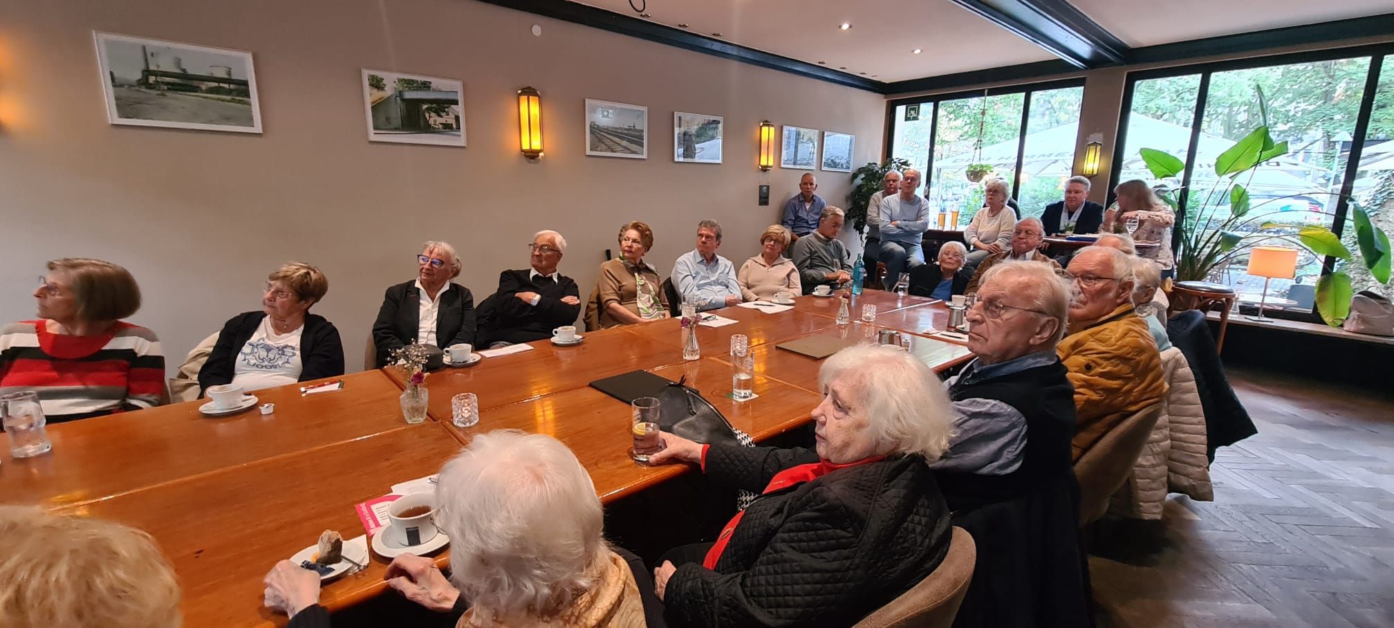 Gruppe älterer Menschen bei geselligem Beisammensein an einem langen Tisch.