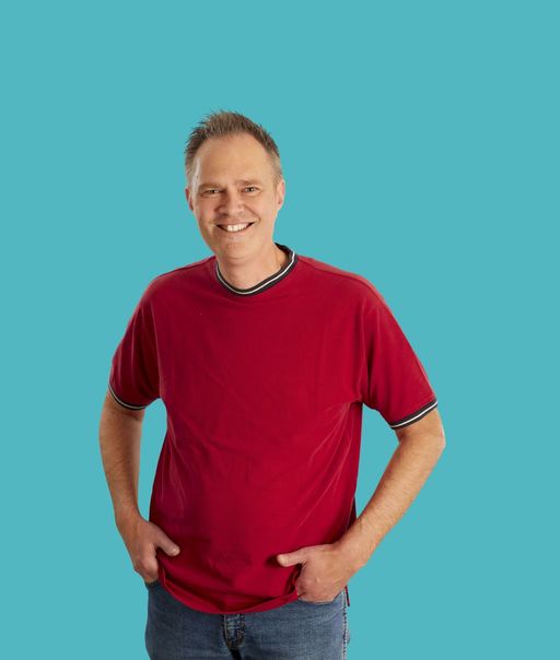 Fröhlicher Mann mit rotem T-Shirt und Jeans, lächelt in den Kamera.